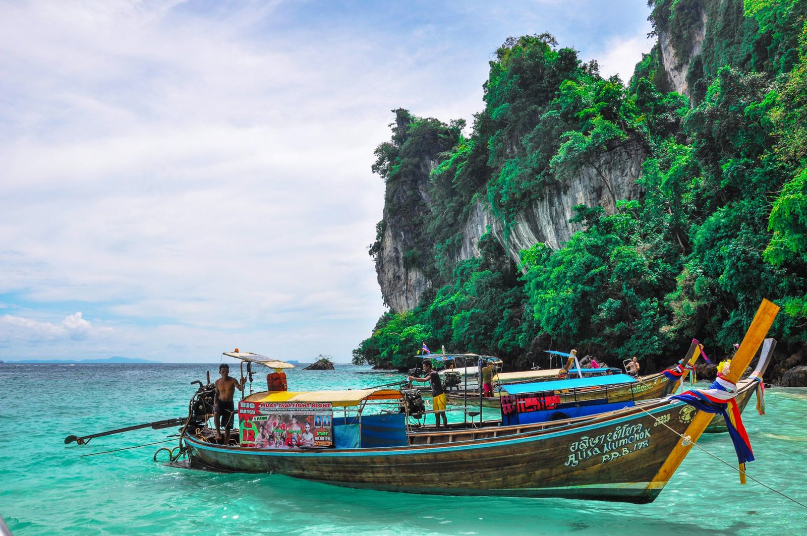 Traditional longtail boat moored in turquoise waters near limestone cliffs in Phang Nga, Thailand